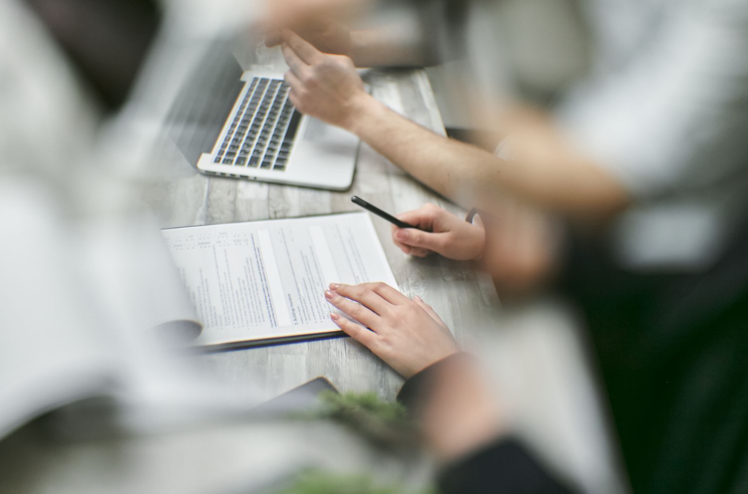 Close view of two people reviewing a printed report at a table, one holding a pen, a laptop beside them.