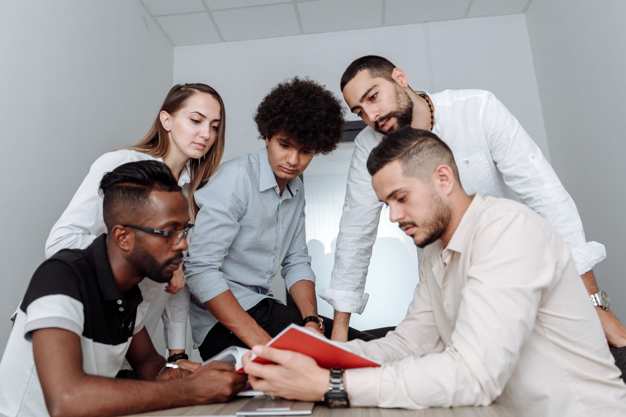 Five colleagues from different backgrounds gathered closely, focused on a document one of them is holding.