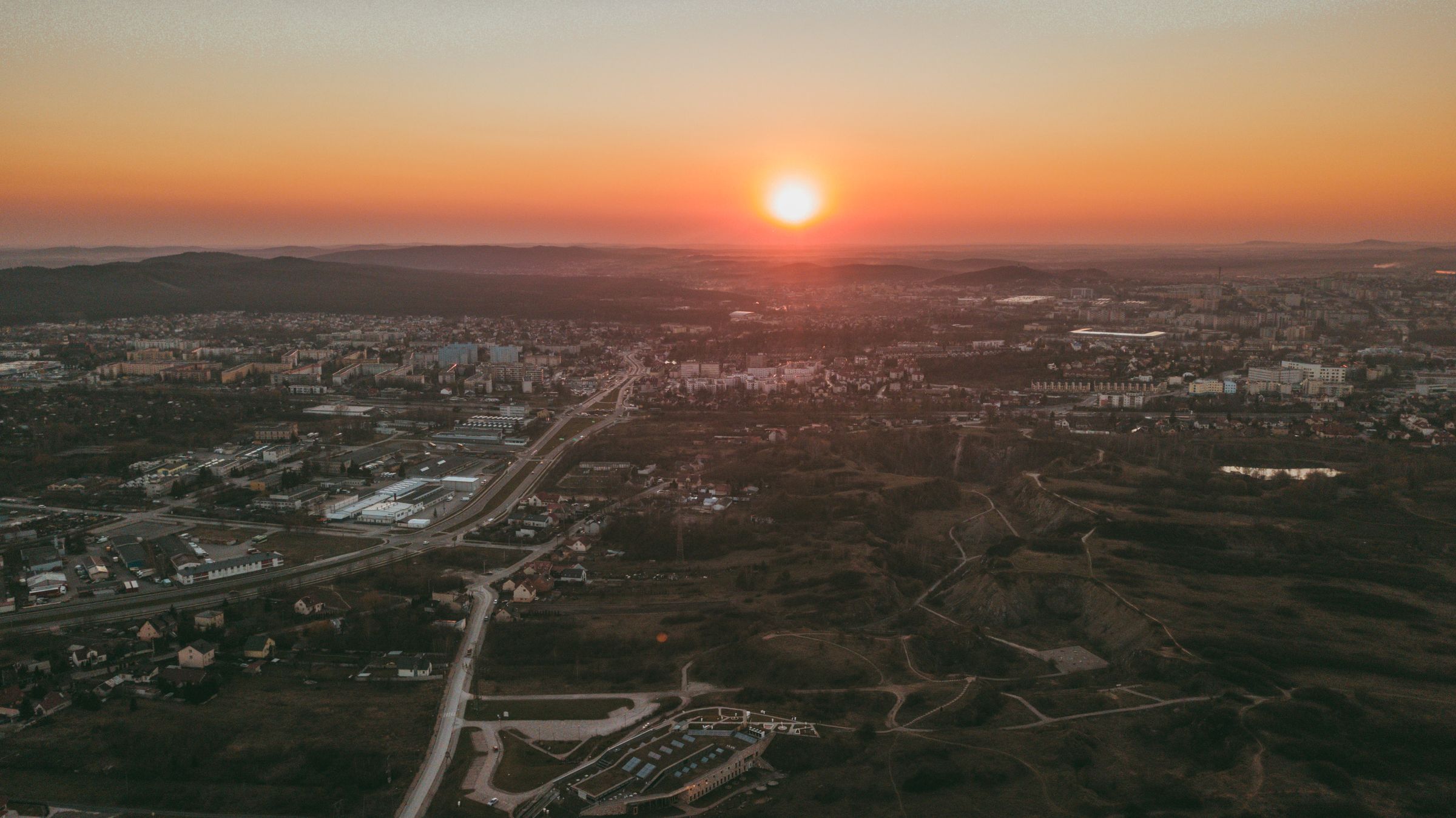Aerial view of a town at sunset, warm light across streets, buildings and hills on the horizon.