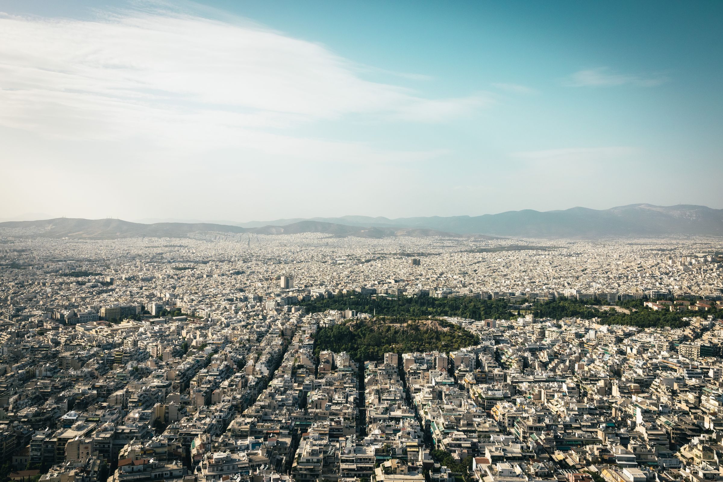 A wide cityscape seen from above, dense low-rise buildings stretching to a line of mountains under a pale sky.